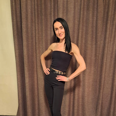 Klientes foto no atsauksmēm: sieviete ar gariem tumšiem matiem melnā tērpā pozē pie aizkariem.